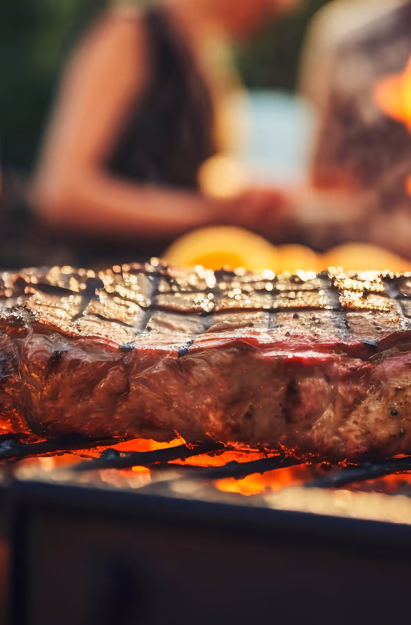 Close-up of a thick steak grilling on a barbecue with glowing coals beneath.
